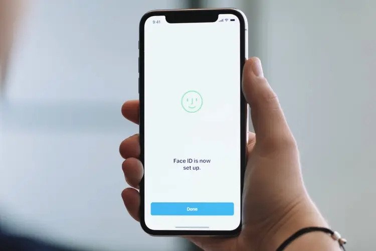 Một người cầm điện thoại iPhone với màn hình hiển thị thông báo "Face ID is now set up